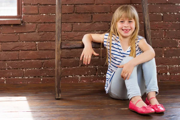 Niña de 6 años se sienta en el suelo junto a una pared de ladrillo y se llena de risa —  Fotos de Stock