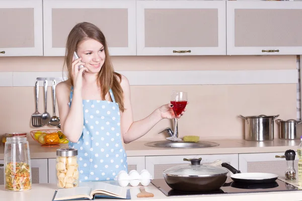 Κορίτσι στην κουζίνα με το ποτήρι κόκκινο κρασί στο τηλέφωνο — Φωτογραφία Αρχείου