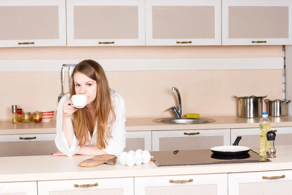 Girl a white men's shirt is drinking tea elbows on table in kitchen the morning — Stock Photo, Image