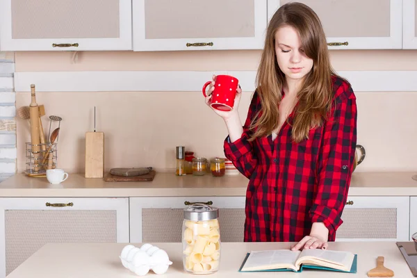 Una chica con una camisa roja de hombre. cocina con taza sus manos —  Fotos de Stock