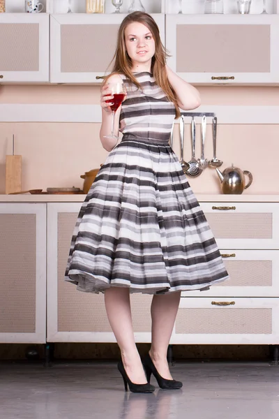 Vestido jovem atraente segurando um copo de vinho em sua cozinha . — Fotografia de Stock
