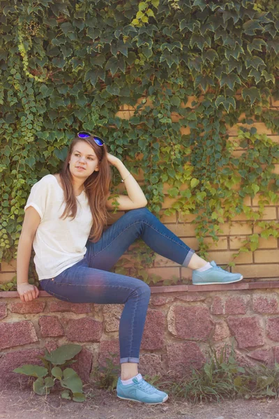 Ragazza seduta sotto il muro con le foglie — Foto Stock