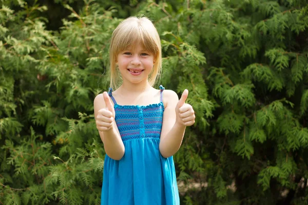 Meisje 5 jaar oud in blauwe jurk toont duimen — Stockfoto