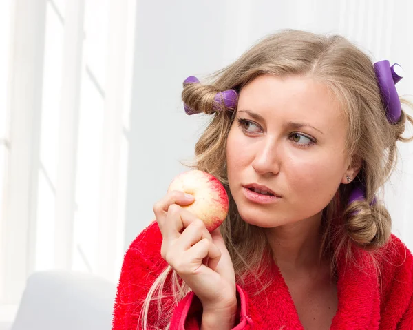 Mädchen in rotem Gewand und Lockenwickler essen einen Apfel — Stockfoto