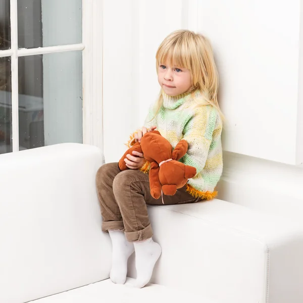 Smiling little girl with teddy bear sitting on sofa home — Stock Photo, Image