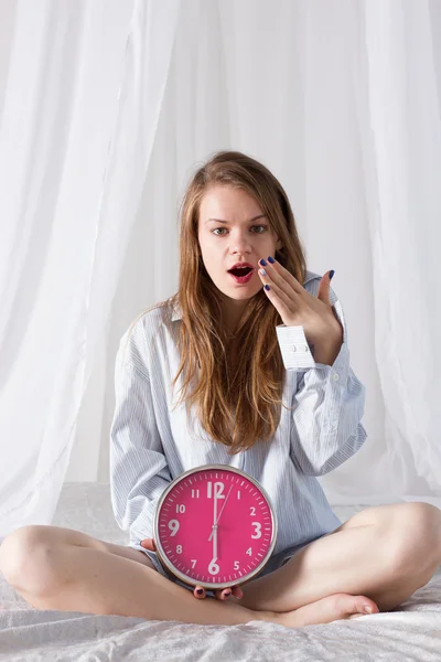 Girl is sitting on bed with big pink clock. 6 a.m — Zdjęcie stockowe