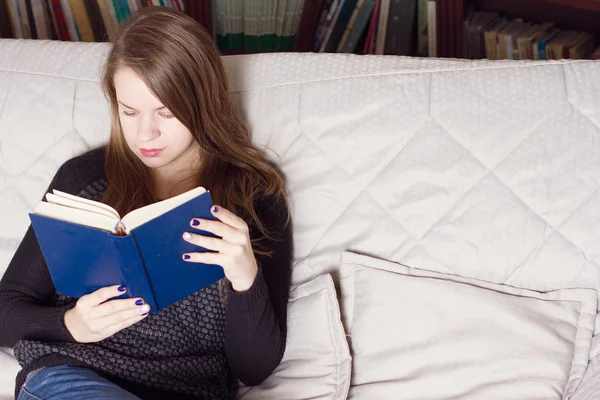 Jovem mulher lendo um livro no sofá — Fotografia de Stock