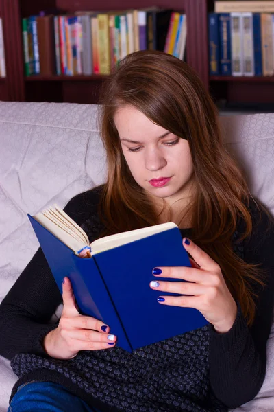 Jovem mulher sentada no sofá em casa, lendo um livro — Fotografia de Stock