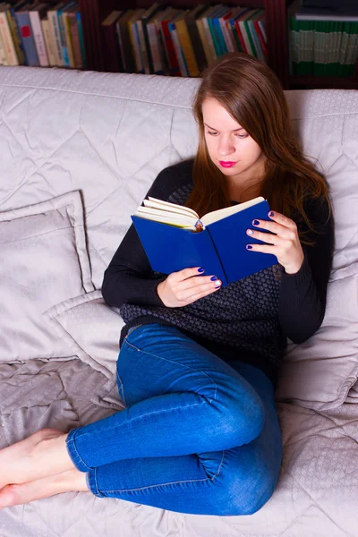 Молода жінка сидить на дивані вдома, читаючи книгу — стокове фото