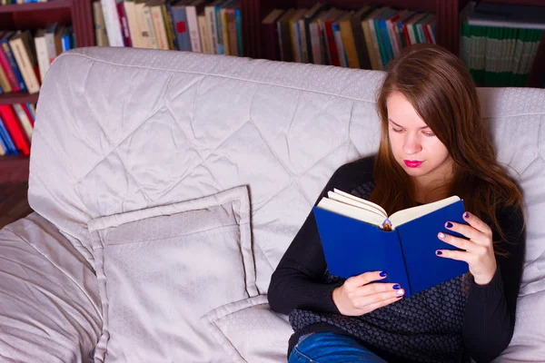 Νεαρή γυναίκα που κάθεται στον καναπέ στο σπίτι, διαβάζοντας ένα βιβλίο — Φωτογραφία Αρχείου