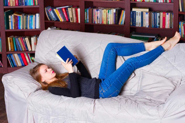 Bela menina leitura livro no sofá — Fotografia de Stock