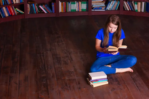 Menina senta-se no chão na biblioteca — Fotografia de Stock