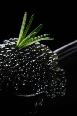 Arka planda yeşil taze biberiye bulunan metal bir kapta siyah havyar.