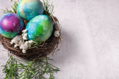 Esrarengiz Paskalya yumurtaları, ince dallar ve bahar çiçekleri ile gri taştan bir arka planda dekoratif bir yuva..