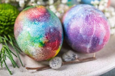 Taş zeminde renkli yumurta ve çiçeklerle dekoratif yuvarlak paskalya tabağı.