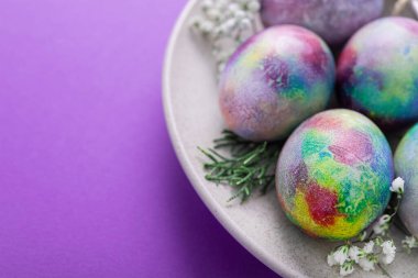 Paskalya tabağında yumurta ve çiçeklerle servis edilen menekşe rengi arka plan.