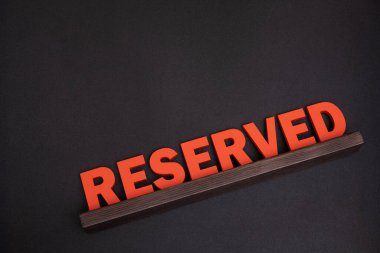 Restoran masasında servis rezervasyonu. Ahşap harfli büyük kırmızı tabela. Üst Manzara. Siyah arkaplan.