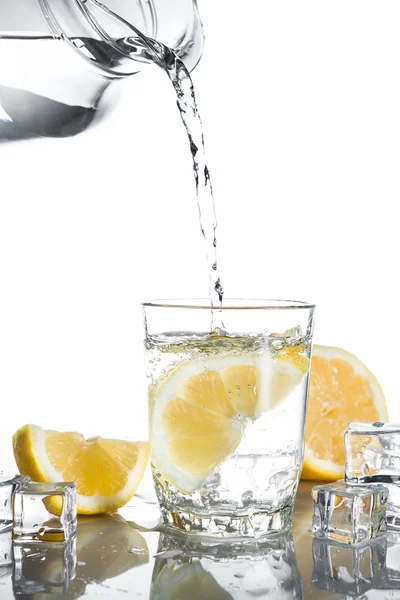 Pouring water into glass with lemons and ice — Stock Photo, Image