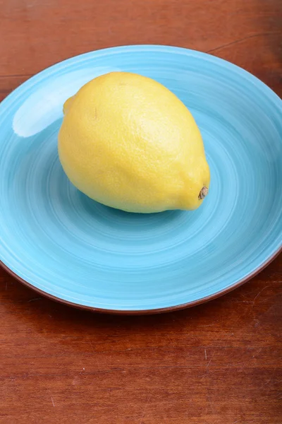 Whole lemon on a blue plate on wooden background — Stock Photo, Image