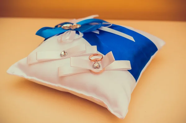 Due fedi nuziali d'oro distese sul bianco con cuscino blu — Foto Stock