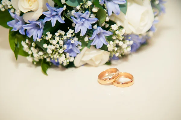 Alianças de casamento em um fundo branco com um buquê de fita azul — Fotografia de Stock