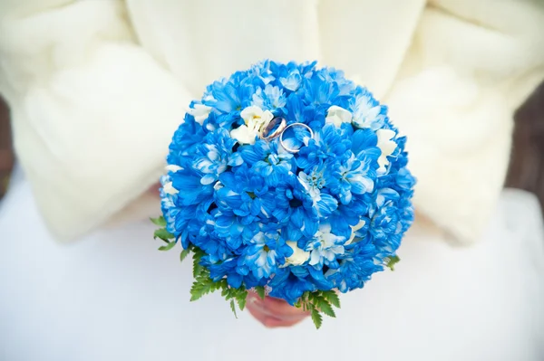 Bride in a fur coat holding a bouquet which lie wedding rings — Stock Photo, Image