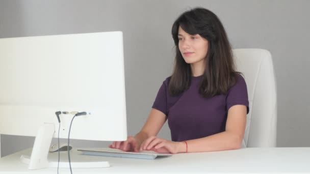 Fotografía media de una chica sentada escribiendo en un lugar de trabajo en una computadora — Vídeo de stock