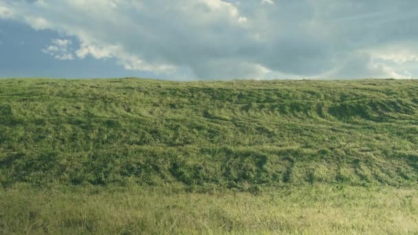 A menina caminha na grama e gira contra o fundo de uma colina verde e céu azul — Vídeo de Stock