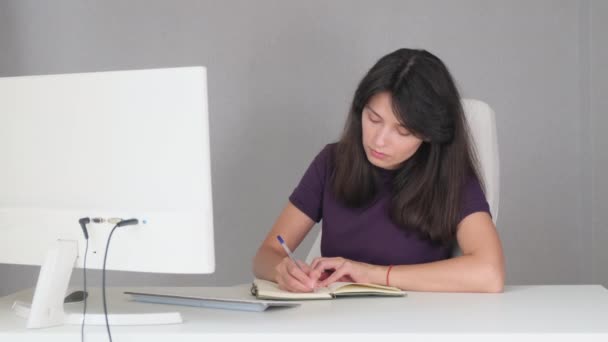 Средний снимок девушки, сидящей за белым столом и пишущей текст — стоковое видео
