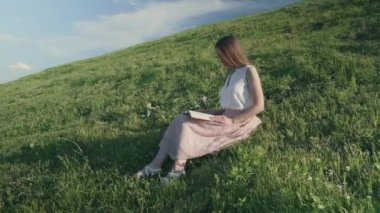 Tepede oturmuş kitap okuyan bir kızın orta boy fotoğrafı.