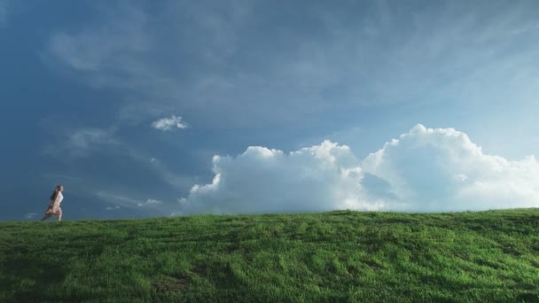 Menina corre em uma colina verde contra um céu azul — Vídeo de Stock