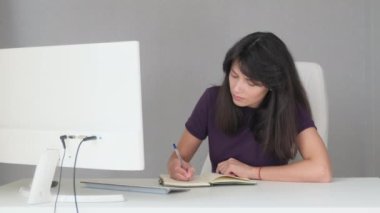 Medium shot of a girl sitting at a white table writing text quickly