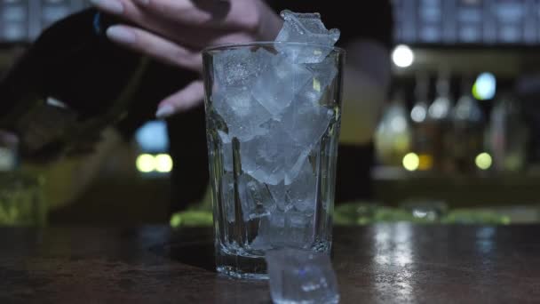 Il barista prepara un cocktail. Mette il ghiaccio in un bicchiere, versa gli ingredienti per un cocktail blu e mette sopra una fetta d'arancia, e poi mescola tutto.. — Video Stock