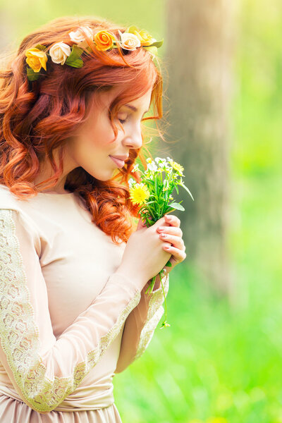 Portrait of a beautiful gentle woman in a forest, female enjoying aroma of a little bouquet of wild flowers, beauty of spring natur