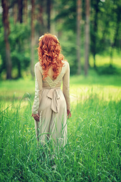 Rear view of a gentle redhead woman in the forest, wearing elegant long dress, fairy tale, romantic fashion look