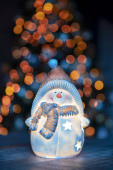 Malá dekorativní sněhulák hračka na stole přes zářící vánoční strom pozadí, šťastný zimní prázdniny, tradiční Nový rok a zimní charakter
