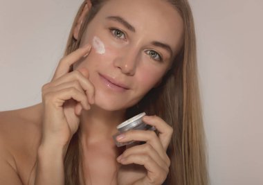 Nemlendirici krem kullanan güzel bir kadın modelinin portresi. Bej arka planda izole edilmiş. Doğal Kozmetik. Güzellik ve Gençlik Konsepti