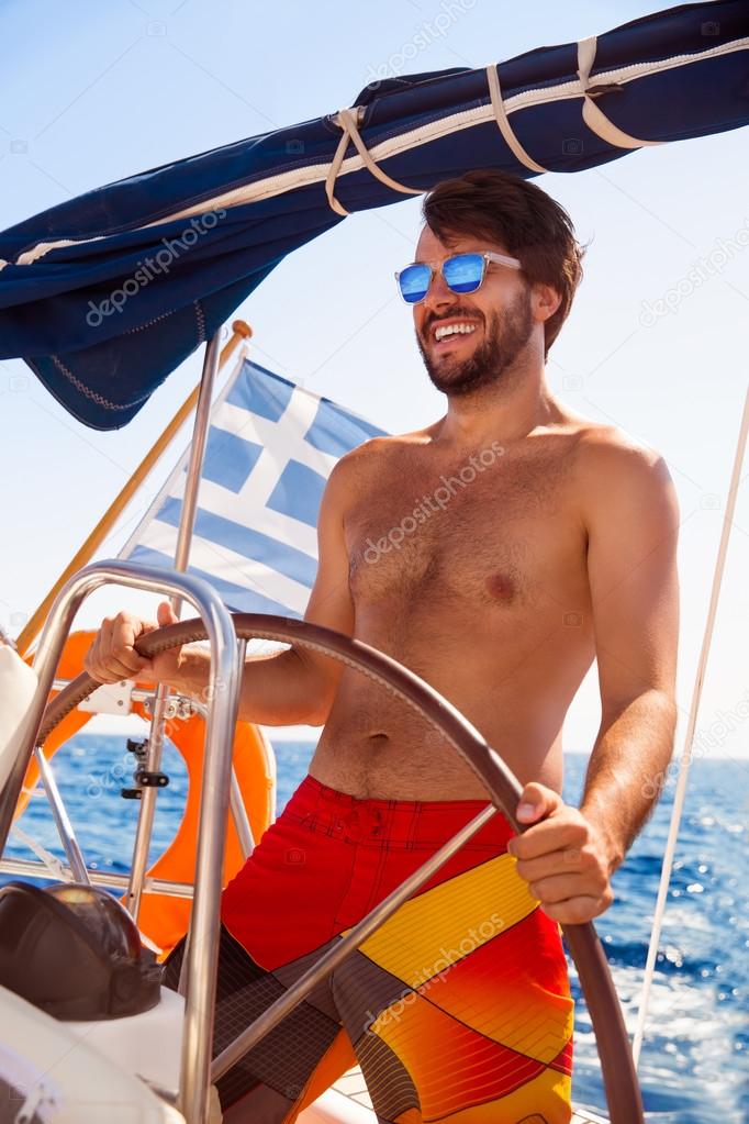 Happy guy behind wheel of sailboat