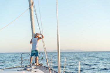 Bir denizci, teknesinde güzel, sakin bir sabahın tadını çıkarıyor. Denizin huzurlu manzarasına bakıyor.