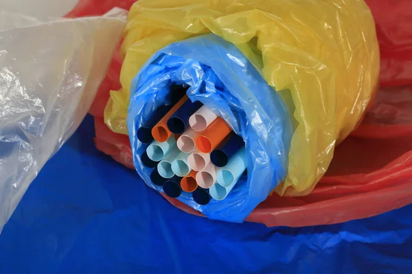 Drinking straw and crumpled plastic material. Plastic disposable items are comfortable and easy to use but the material they are made of seriously pollutes the environment.