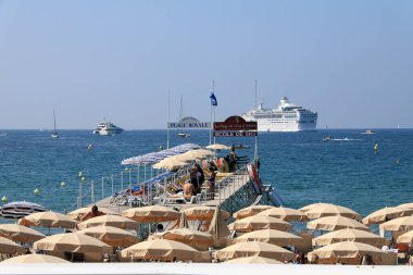 Cannes, Fransa - 5 Temmuz 2009: Akdeniz sahilindeki şemsiyeler. Ayrıca küçük bir rıhtım ve denizde tekneler, yatlar ve bir yolcu gemisi var..