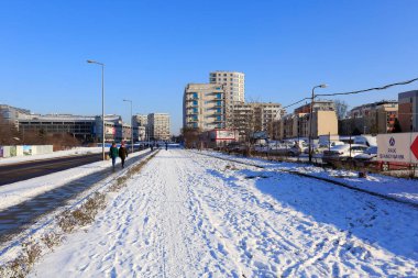 Varşova, Polonya - 31 Ocak 2021: Kent sokağı, kaldırım ve karla kaplı hem bisiklet yolu hem de yakınlardaki çimenler. Goclaw konutlarında bir otopark ve binalar var..