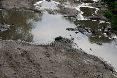 Toprak yolda çamur birikintisi ve lastik izleri var.