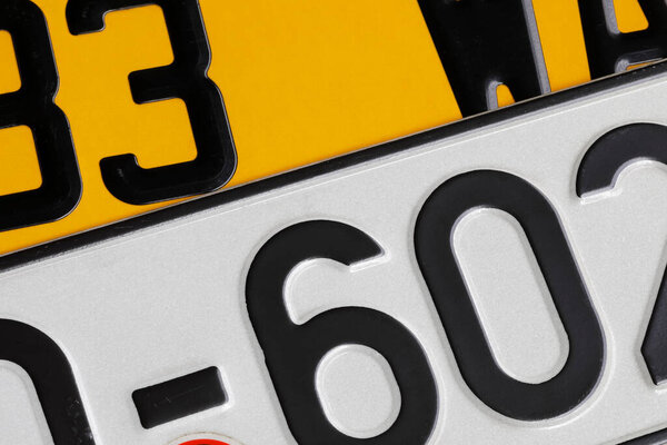 Vehicle license plates with numbers and letters on them. The different colors result not only from their country of origin but also from the purpose of the vehicle on which they are placed.