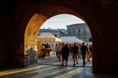 Lublin, Polonya - 10 Eylül 2021: Bilinmeyen insanlar ünlü Krakow Şehir Kapısı 'ndan geçerek geniş geçitte yürüyorlar. Kapıdaki tezgahlarla perakende alanının arkasında....