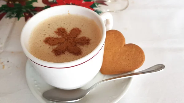 cup of coffee with milk and a drawing with cinnamon next to a cookie