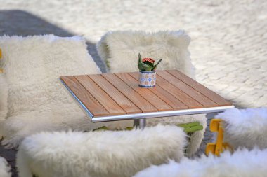 İsviçre, Zürih 'te parlak güneş ışığı altında tüylü beyaz koyun postlarıyla örtülmüş sandalyelerle çevrili Eski Şehir meydanında bir açık kafeterya masası.