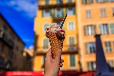 Ellerinde zanaat çikolatası ve arena vişneli dondurma, geleneksel renkli evler manzarası, Old Town Vieille Ville, Nice, Güney Fransa