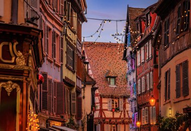 Tarihi yarım ahşap evlerdeki şenlikli dekorasyon ve süsler Eski Şehir, Colmar, Alsace, Fransa 'daki Noel Pazarı sırasında gün batımında parlıyor.