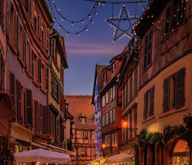 Tarihi yarım ahşap evlerdeki şenlikli dekorasyon ve süsler Eski Şehir, Colmar, Alsace, Fransa 'daki Noel Pazarı sırasında gün batımında parlıyor.